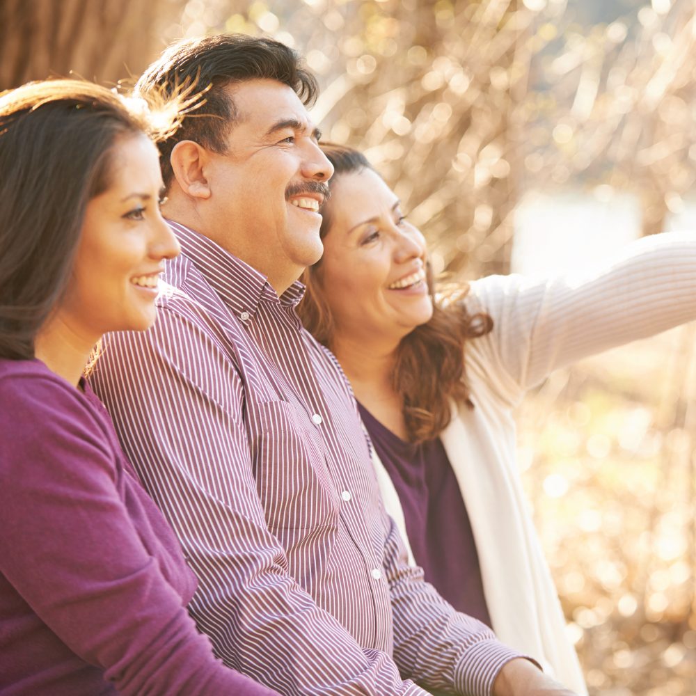 An Hispanic man with his wife and daughter smiling together outside